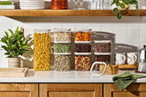 Naked Kitchen glass canisters with cream lids organizing pantry staples on a styled kitchen counter with plants and a moka pot