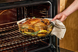 Person taking a roasted chicken out of an oven using a Naked Kitchen glass dish.