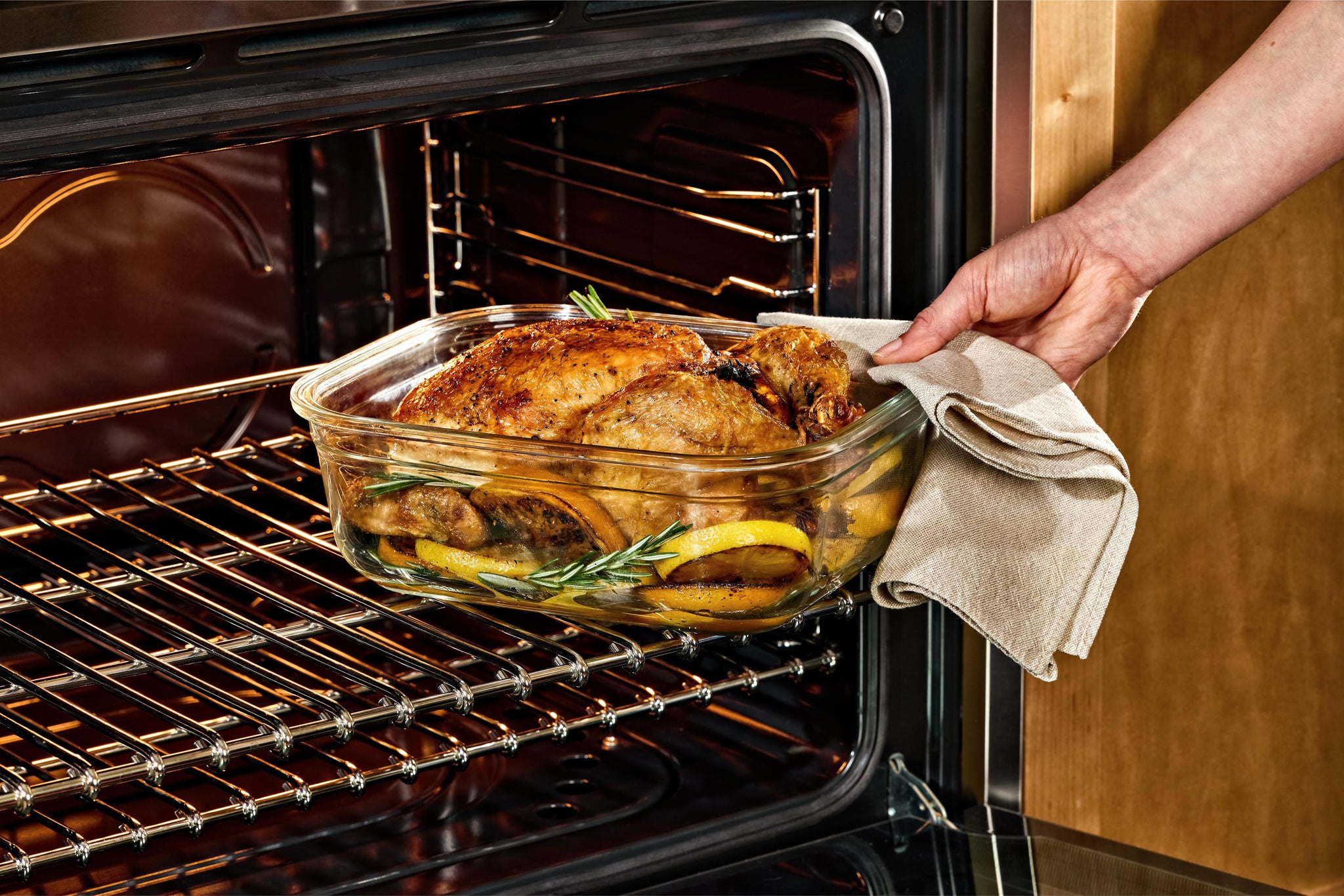 Person taking a roasted chicken out of an oven using a Naked Kitchen glass dish.