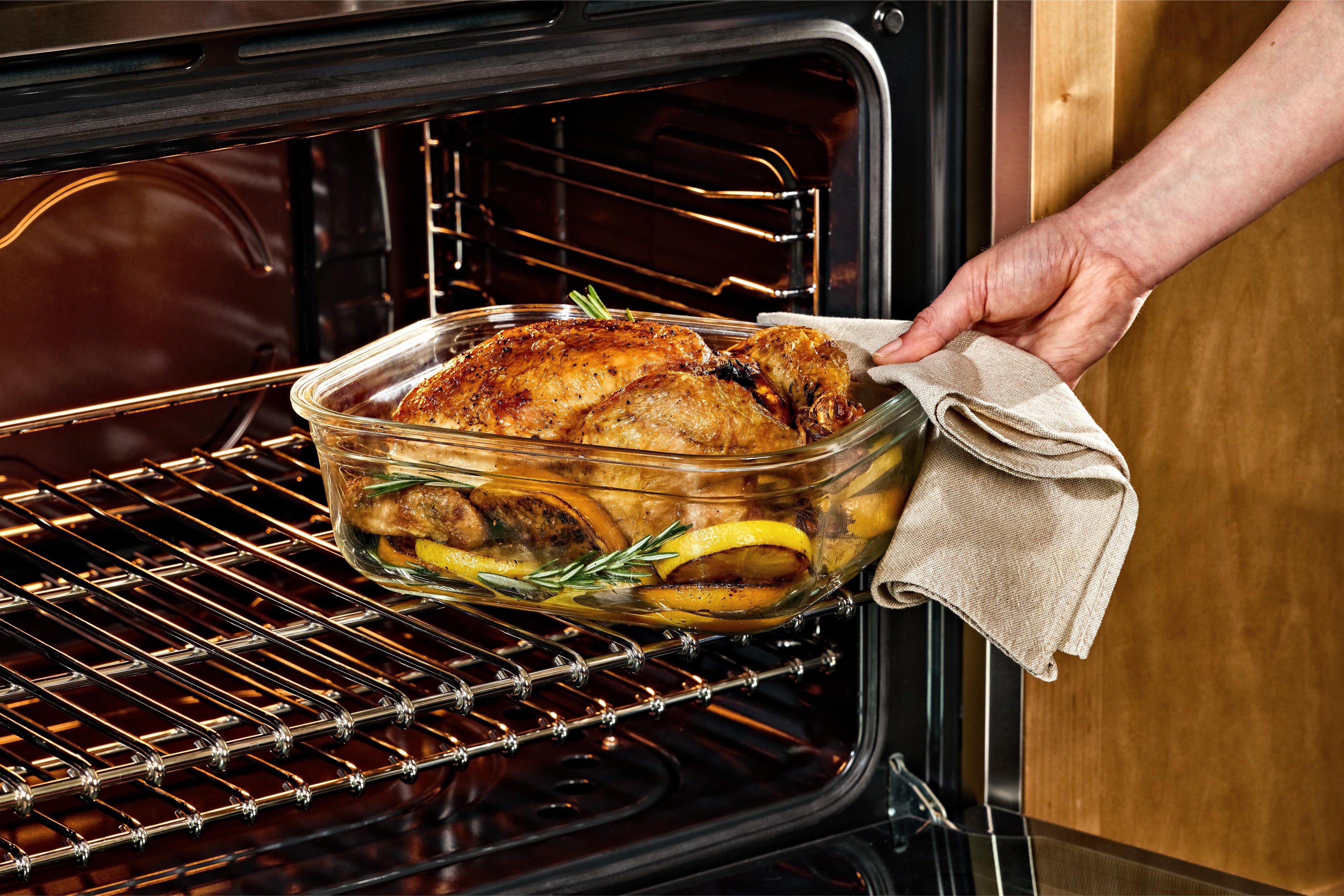 Person taking a roasted chicken out of an oven using a Naked Kitchen glass dish.
